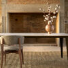 Table artisanale céramique Dekton modèle Comtesse ARTMETA 4K vue devant cheminée Table céramique Dekton modèle Comtesse / Dimensions : 200x100xH75 cm / Plateau : Entzo Pieds : Bronze / Fabrication ARTMETA